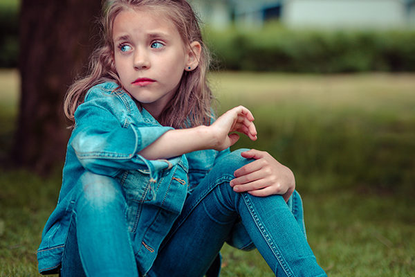 Young girl sitting on the ground outside looking worried and anxious